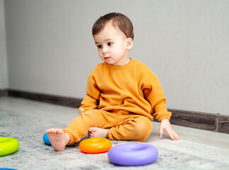 Small kid playing on the floor indoor. Adorable young boy sitting with colorful toys.