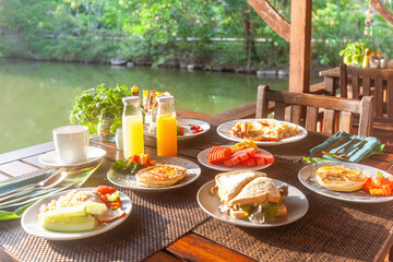 Enjoy a tasty breakfast by the lake at a Thailand resort. Savor fresh dishes like fried eggs, toast, and organic orange juice. Perfect start to a summer vacation.