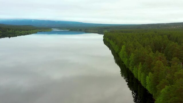 Aerial over the smooth reflective surface of a lake amid the Pine forests and mountains near Hedmark, Norway. Drone orbit shot