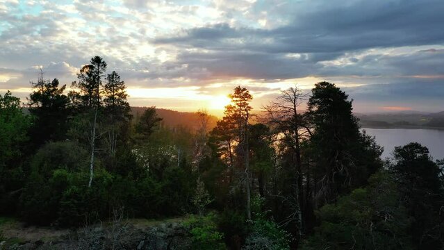 Sunset falls behind the mountains and trees near Toensberg, Norway. Drone crane upward shot