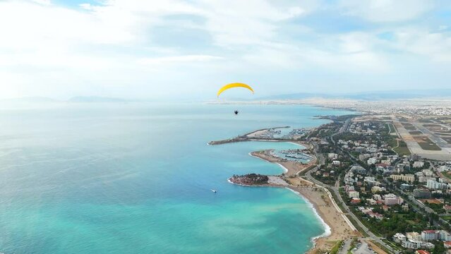Drone follow Powered paraglider flyover turquoise water by Glyfada Coastline, Greece