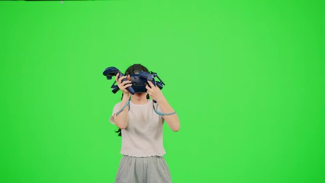 The little girl wearing VR headset gaming in virtual reality. The child gaming on chroma key green screen background in virtual reality. Concept game in VR headset leisure activity virtual reality