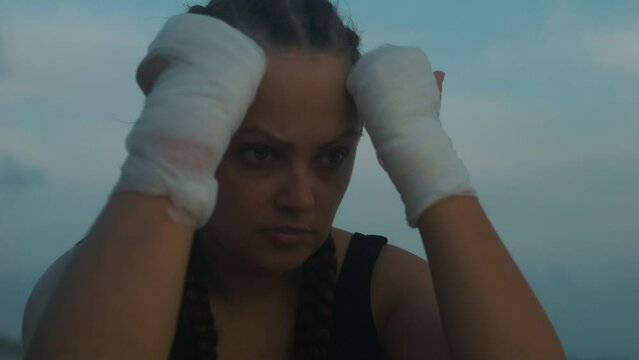 Sad female boxer MMA fighter on beach looks into distance with head in hands.