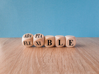 Adaptable or flexible symbol. Turned wooden cubes and changes the word Adaptable to Flexible. Beautiful wooden table, blue background, copy space. Business, adaptable or flexible concept.
