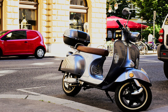 retro style metallic japanese scooter or moped parked on asphalt road. and sidewalk old stucco house exterior wall. classic building elevation. large arched windows. modern transportation style