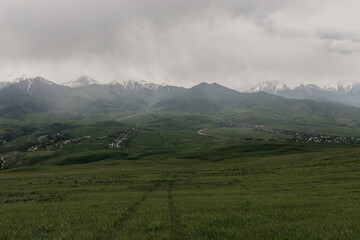 A summer view of mountain peaks shrouded in clouds and a distant village