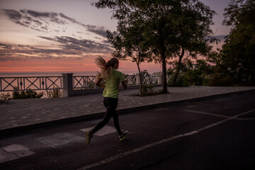 Young woman in sportswear runs along the path at dawn. Morning routine, meditation, feeling of freedom. Girl is wearing black leggings and a yellow T-shirt. Beautiful red sky. Concentrated motivation