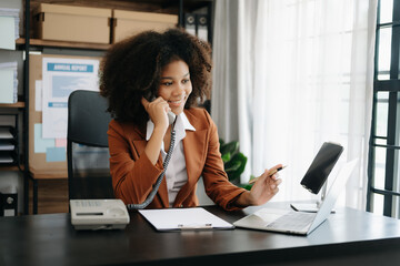 Business African woman Talking on the phone and using a laptop with a smile while sitting at office