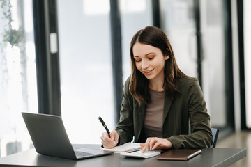 Business Caucasian woman Talking on the phone and using a laptop with a smile while sitting at modern office