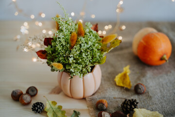 Autumn composition of pumpkins, nuts, autumn leaves, a bouquet of dried flowers, cones. Pumpkin and nuts. Garland with warm light. Yellow Bokeh. Thanksgiving Day.