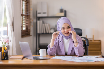 A stressed Asian business asian islamic woman in hijab holding documents is working from home, feeling stressed because of lot of paperwork appearing worried, tired, and overwhelmed