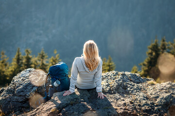 Woman with backpack resting on rock after successfully climbed mountain summit