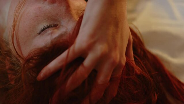 Beautiful ginger woman playing with her hair and moaning while she lays in bed and caresses her body