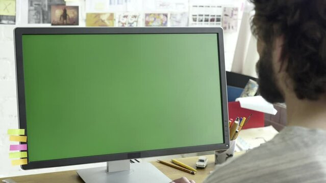 Green screen computer display placed on wooden table in working room. Adult caucasian male working in front of monitor. Typing on the keyboard while writing code, text, copywriting, chatting.