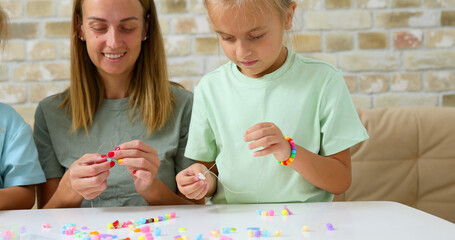 Happy mother with her daughters making beaded jewelry at home