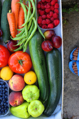 Crate of fresh fruit and vegetable, picked from the garden, and feet in blue sandals. Summer in the garden concept. Top view, unrecognizable person.
