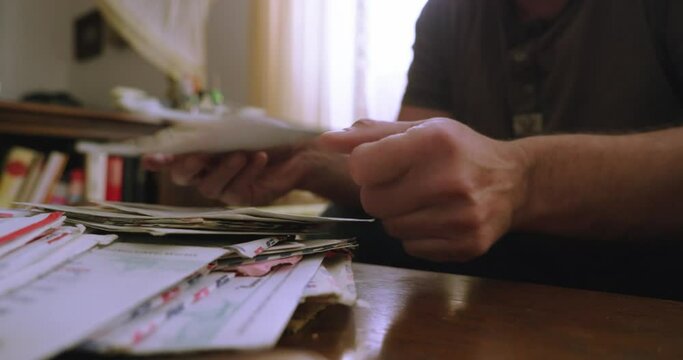 A person's hands search for a letter in a pile of correspondence made up of letters and envelopes