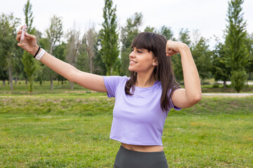Smiling sport woman taking a selfie with smartphone after fitness training outdoors. Proud beautiful young female athlete workout. Running, wellness, exercise, health and active lifestyle.