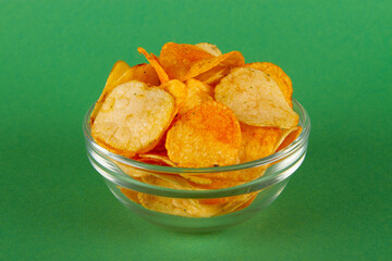 Potato chips in glass bowl isolated on green background. SIDE view