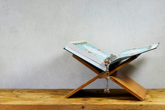 Mawlid Al Nabi Or Ramadan, Eid Concept.  Muslim Book With Arabic Calligraphy Quran - Translation : The Noble Book Of Muslims Around The World On Stand And Rosary On Wooden Board