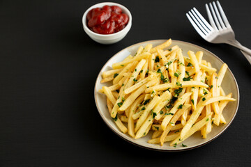 Garlic French Fries with Parsley on a Plate on a black background, side view.