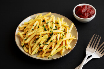 Garlic French Fries with Parsley on a Plate on a black background, side view.
