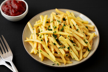 Garlic French Fries with Parsley on a Plate on a black background, side view. Close-up.