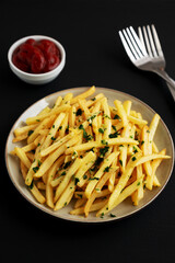 Garlic French Fries with Parsley on a Plate on a black background, side view. Close-up.