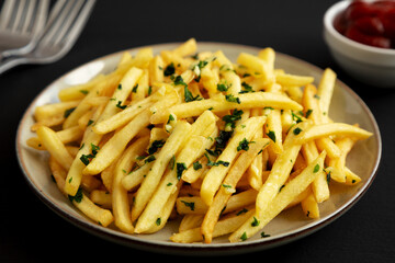 Garlic French Fries with Parsley on a Plate on a black background, side view. Close-up.