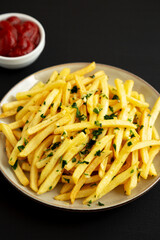 Garlic French Fries with Parsley on a Plate on a black background, side view. Close-up.