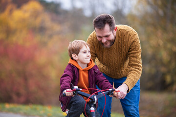 Father teaching his little son to ride bicycle in park. Bearded man helping child to learn bike. Family values, child support, fathers day concept. Selective focus.