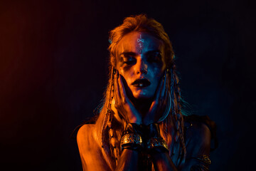 Portrait of bloody body art mysterious valkyrie hands touch face orange light isolated on black color background