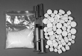 A close-up with a plastic bag with white powder, syringes and pills in black and white