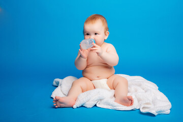 baby in a diaper sitting on a blue background drinking from a bottle, high quality photos