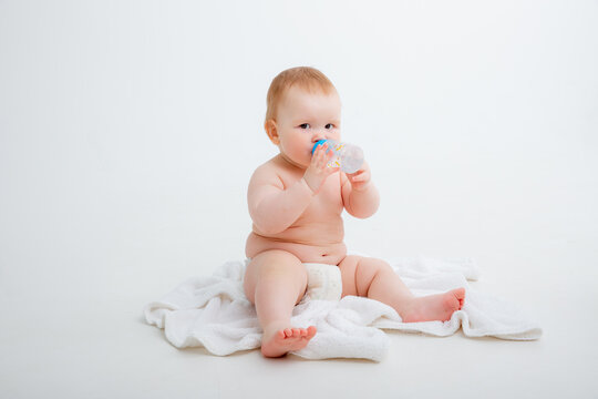 baby in a diaper sitting on a white background drinking from a bottle, high quality photos