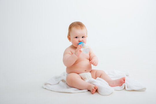 baby in a diaper sitting on a white background drinking from a bottle, high quality photos