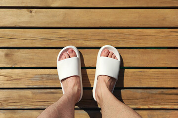 Male feet wearing white slippers on the pier