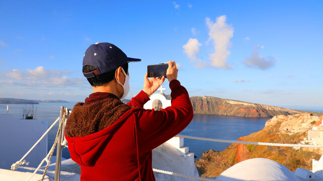 Back view of young tourist man  using smartphone take picture at View of blue church dome in Oia village,Santorini,Greece