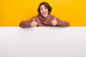 Portrait of crazy funky girl dressed brown sportswear on white placard empty space showing thumbs up isolated on yellow color background