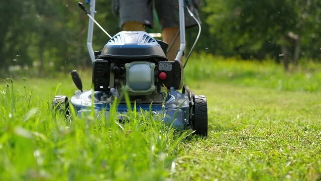 Lawn mower cutting grass. Small grass cuttings fly out of lawnmower. Grass clippings get spewed out of a mower pushed around by landscaper. Slow Motion. CloseUp. Gardener working with mower machine.