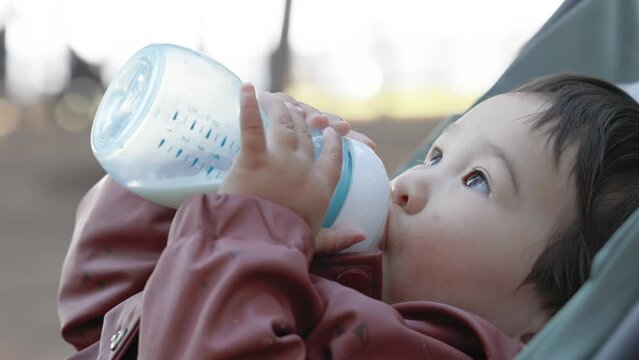 Asian baby drinks formula from a bottle while lying on the stroller in the park