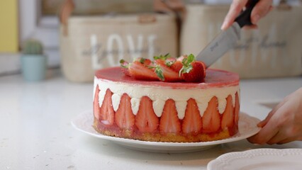 Close-up of a woman's hands cuts a fresh strawberry cake