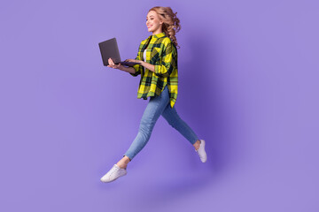 Fototapeta na wymiar Full length photo of sweet excited lady wear plaid yellow shirt jumping high working modern gadget isolated violet color background