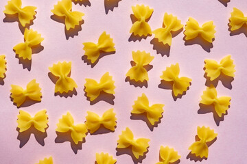 Farfalle pasta pile on pastel pink surface. Cute shape of raw, uncooked pasta on blight pink background.  Italian cuisine.