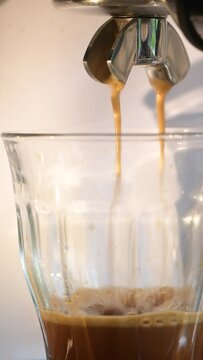 Video von frischem, hei&szlig;em Kaffee, Espresso, Crema l&auml;uft, flie&szlig;t aus der Espressomaschine. Nahaufnahme im Hochformat f&uuml;r Social media. Die selektive Sch&auml;rfe liegt auf dem laufenden Kaffee