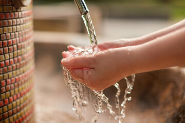 Naklejka na ściany i meble 庭の水道水の蛇口で手洗いしている女性の両手の様子