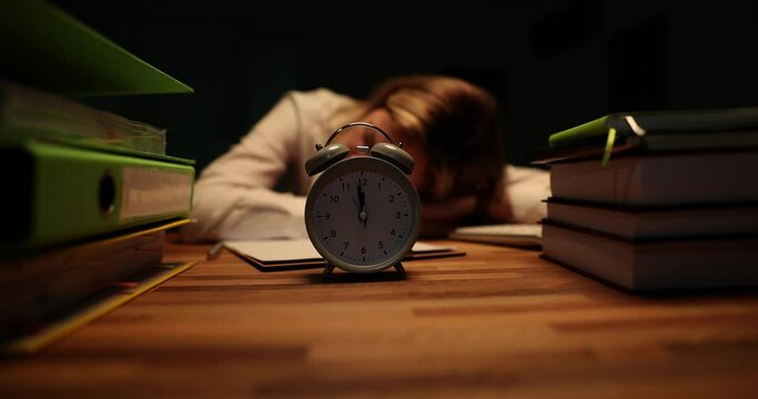 Tired overworked business woman sleeps on office desk in evening with documents and alarm clock. Overtime manager trainee