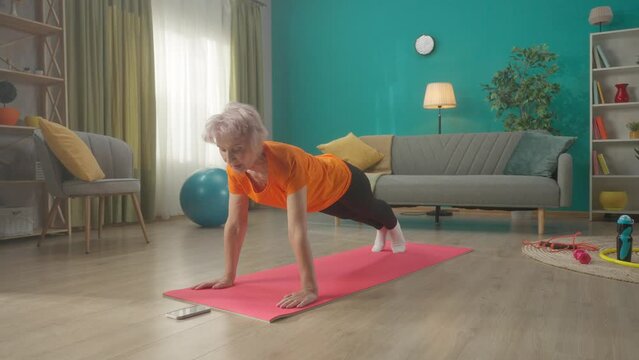 An elderly woman in sportswear lies on the floor in front of the phone. A woman starts a timer on her phone and gets into a plank position. HDR BT2020 HLG Material.