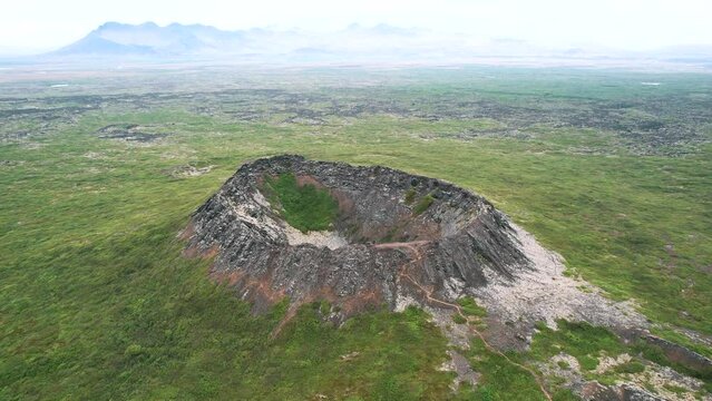 aerial volcano eldborg, push out movement, green summer hazy misty volcanic landscape, shrub spatter cone, touristic trail for outdoor travellers. cinematic drone shot, epic travel destination.