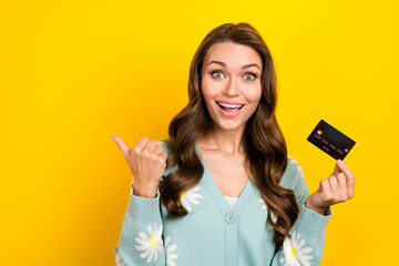Portrait of charming astonished person hold debit card indicate finger empty space isolated on yellow color background